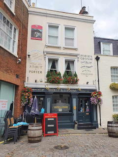 Traditional London pub exterior with flower baskets, painted signs, and cobblestone street