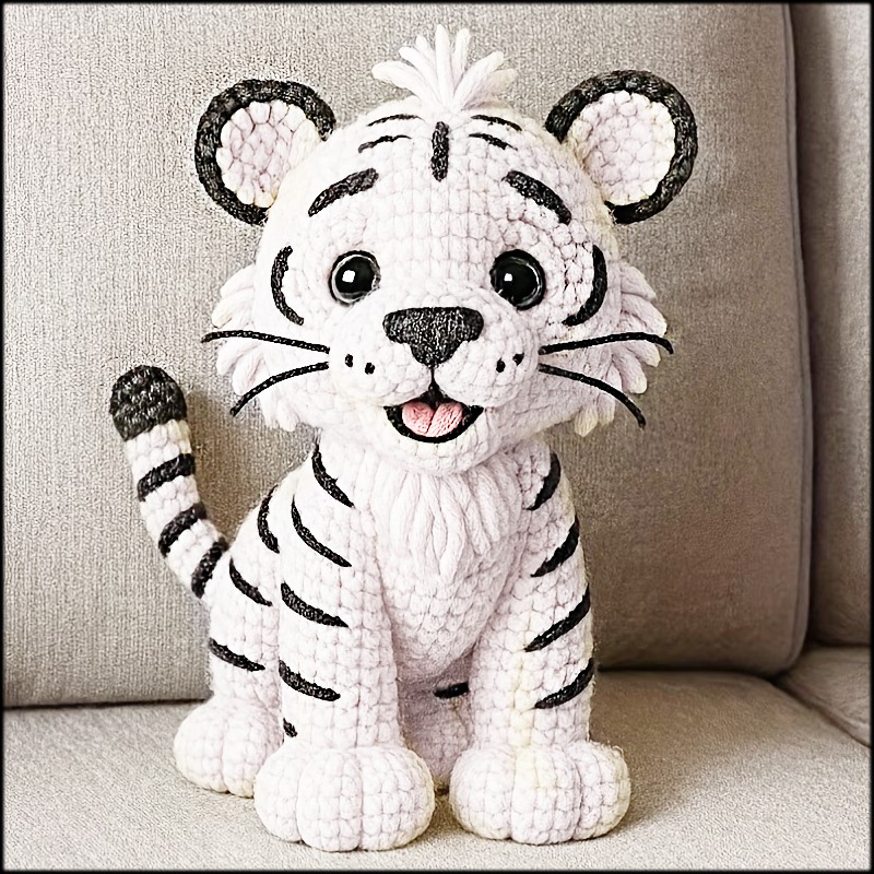 Crocheted white tiger cub plush toy sitting on a beige sofa