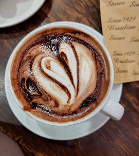White cup of latte with swirled chocolate leaf art pattern on a wooden cafe table