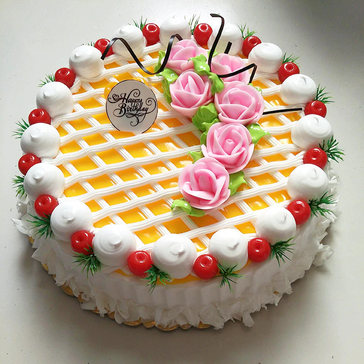 Birthday cake decorated with yellow lattice pattern, pink roses, white cream piping, and strawberries