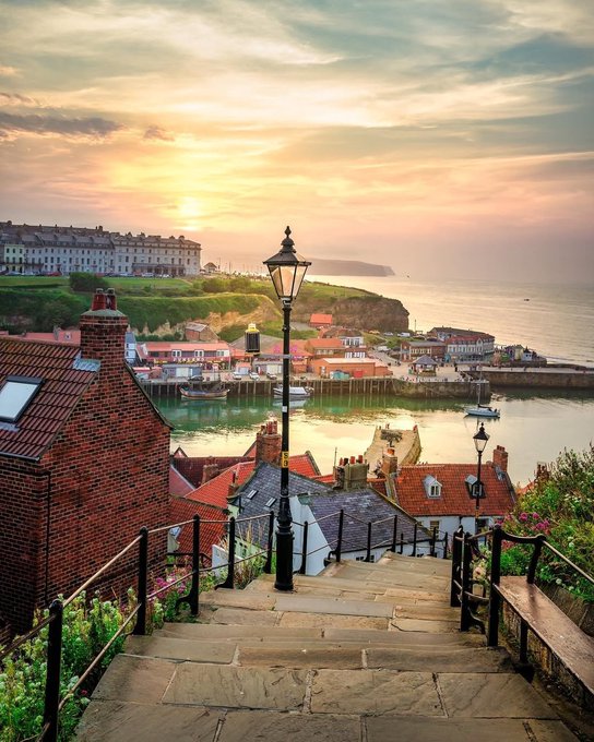 Stone steps leading down to Whitby harbour at sunset, with red-roofed buildings and a lamp post, North Yorkshire