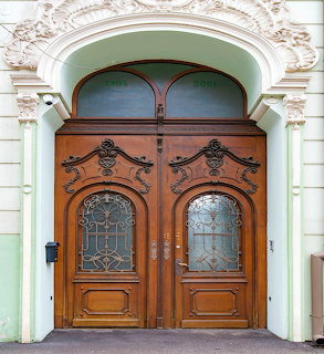 Ornate carved wooden double door with decorative glass panels under an arched facade