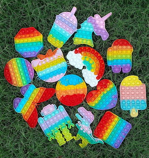 Assorted rainbow-colored pop it fidget toys in fun shapes on green grass
