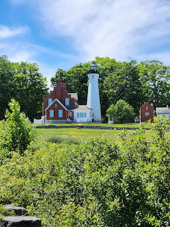 White lighthouse with red brick house amid lush greenery and blue sky
