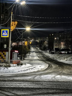 Snowy city street at night with streetlights, buildings, and a winding road