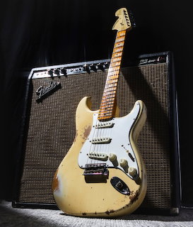 Worn cream Fender Stratocaster guitar leaning against a black amplifier
