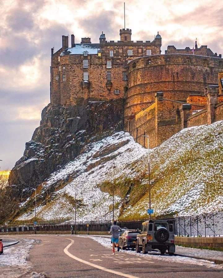 Edinburgh Castle perched on snow-dusted volcanic rock with a road and parked 4x4 vehicle below