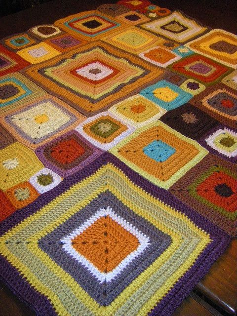 Colorful crochet granny square blanket with autumn-toned squares in various sizes on wooden floor