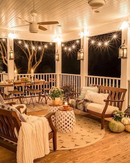 Cozy covered porch at night with string lights, lanterns, wooden furniture, pumpkins, and autumn decor