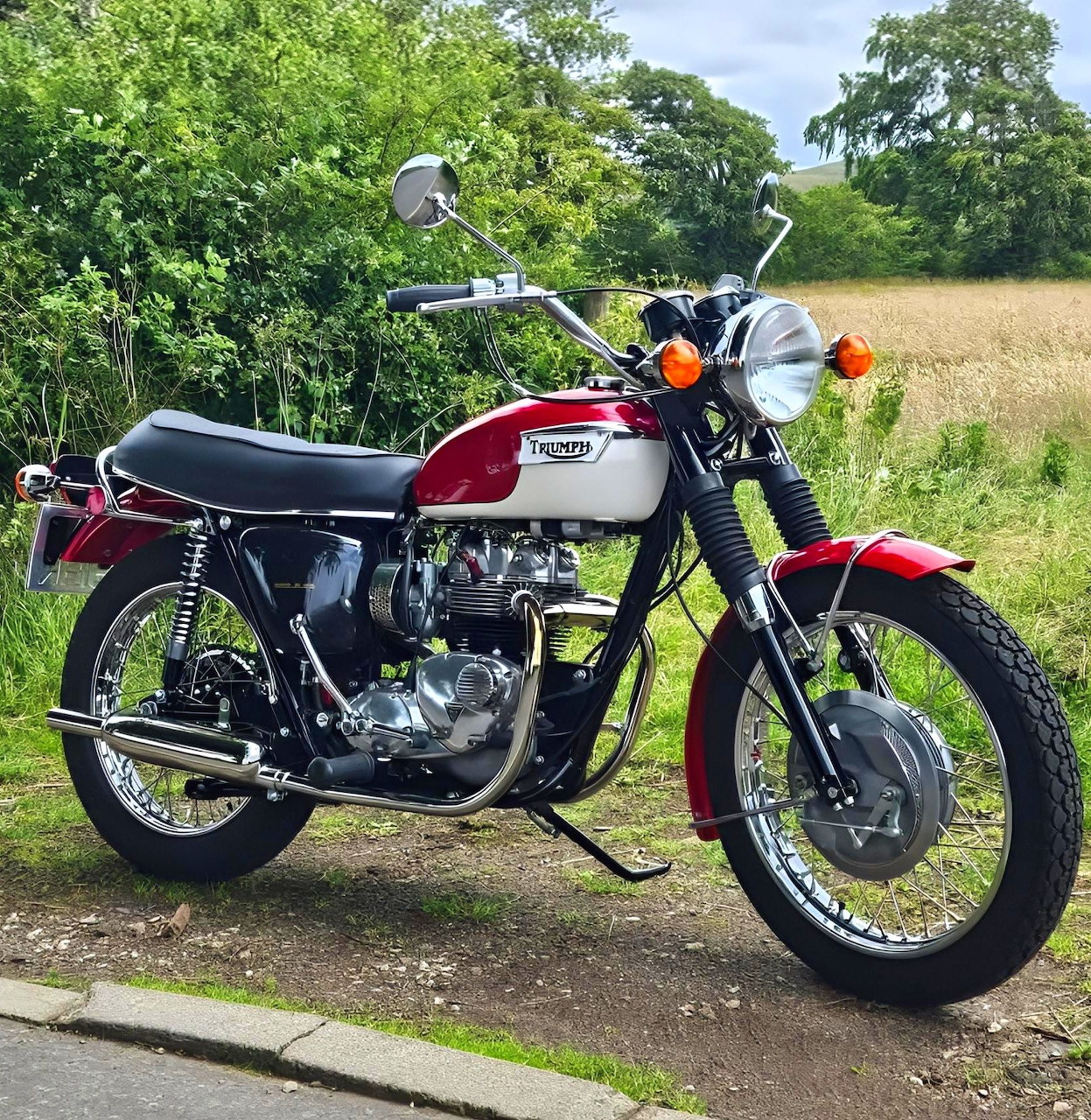 Vintage red and silver Triumph Daytona T100R motorcycle parked by a country roadside