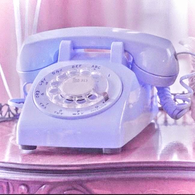 Pastel blue rotary telephone on a glossy table with soft pink and purple lighting