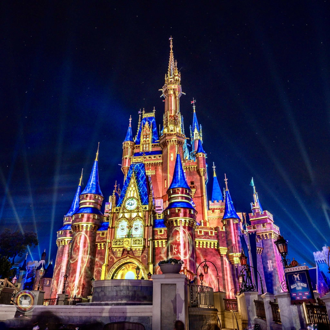 Illuminated fairy tale castle with blue and pink lights under starry night sky with radiating light beams