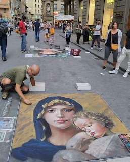 Street artist drawing Madonna and child chalk art on Florence pavement while tourists walk by