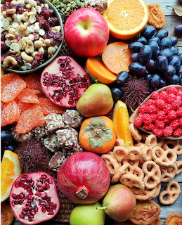 Overhead view of assorted autumn fruits, nuts, and snacks arranged on a wooden board
