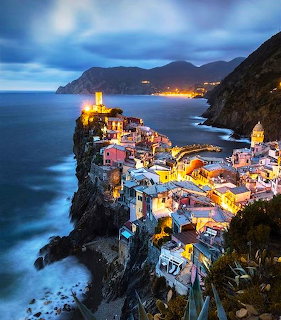 Cliffside village at dusk in Cinque Terre, Italy, with glowing buildings above the sea