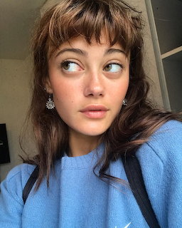 Portrait of young woman with brown hair and bangs in blue sweater looking up