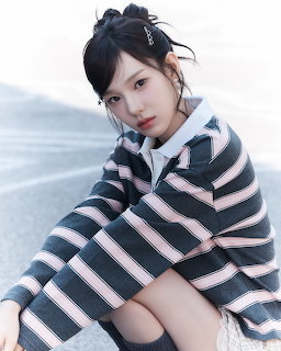 Young Asian woman in striped grey and pink polo sweater sitting outdoors looking at camera