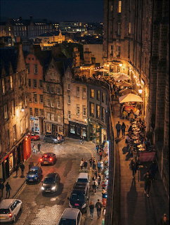 Aerial view of an Edinburgh street at night with warm lighting on historic stone buildings and pedestrians