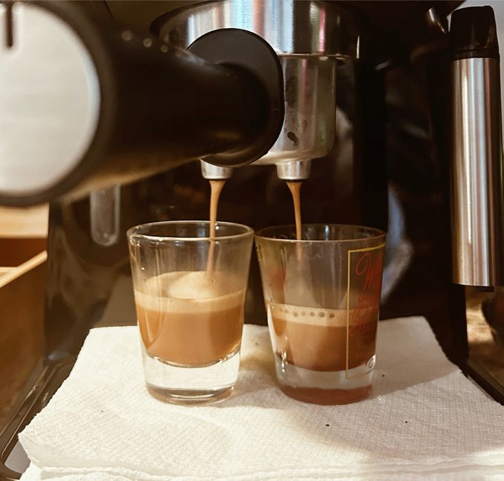 Espresso machine pouring coffee into two glass cups on white surface