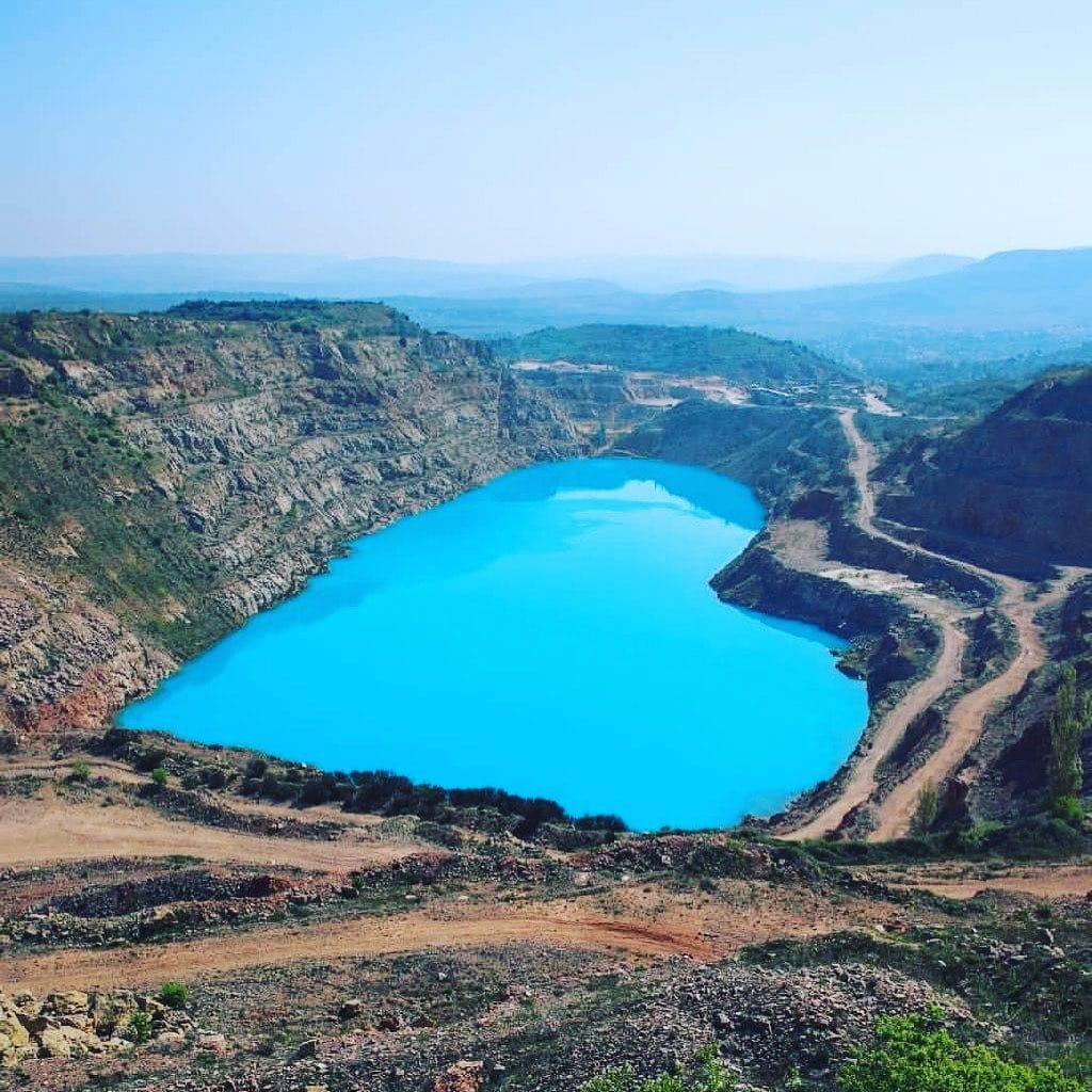 Turquoise lake inside a rocky quarry with steep cliffs and winding dirt roads