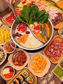 Top-down view of a hot pot meal with meats, vegetables, sushi, fries, and dipping sauces