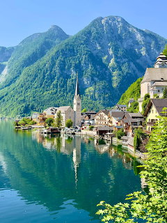 Lakeside village with church spire, calm water reflections, and green mountains
