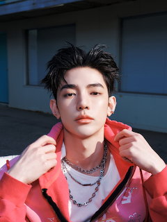 Young man wearing a pink hoodie and chain necklaces, posing indoors
