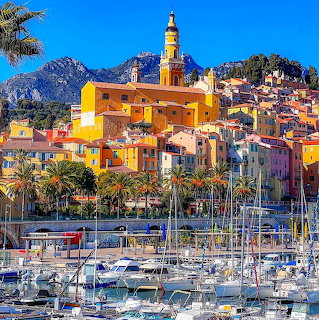 Vibrant coastal town Menton with colorful buildings, bell tower, palm trees, marina, and mountains under blue sky
