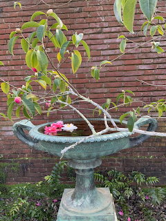 Stone bird bath with pink flowers and branches in front of a brick wall