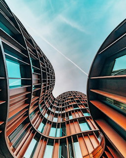 Looking up at curved futuristic buildings with wavy architecture and glass facades against blue sky