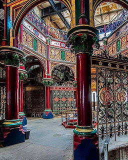 Ornate Victorian arcade with red iron columns, colorful patterned tiles, and decorative arches