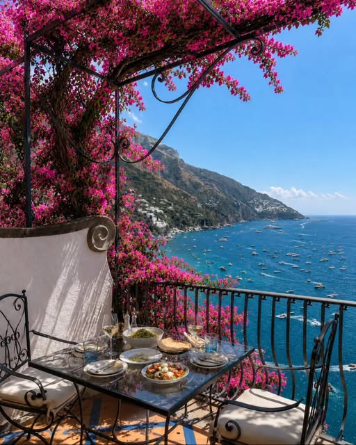 Seaside terrace with table, pink bougainvillea, and blue ocean view along a rocky coast