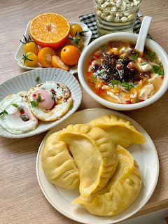 Tabletop meal with steamed dumplings, soup, toast with eggs and ham, and oranges