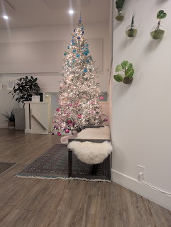 Lit white Christmas tree in modern room corner with gifts and wall plants