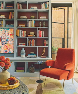 Cozy room with a bookshelf, red armchair, small table, and colorful painting by a window