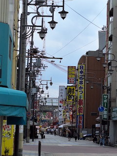 Narrow Japanese city street with signs, power lines, and hanging street lamps between buildings