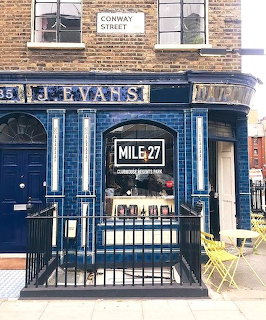 Blue corner cafe entrance with Mile 27 signage, metal railings, and brick upper story
