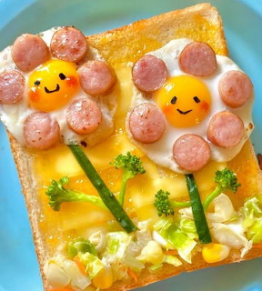 Kawaii toast with two smiley-face eggs and sausage arranged as flowers with vegetable stems