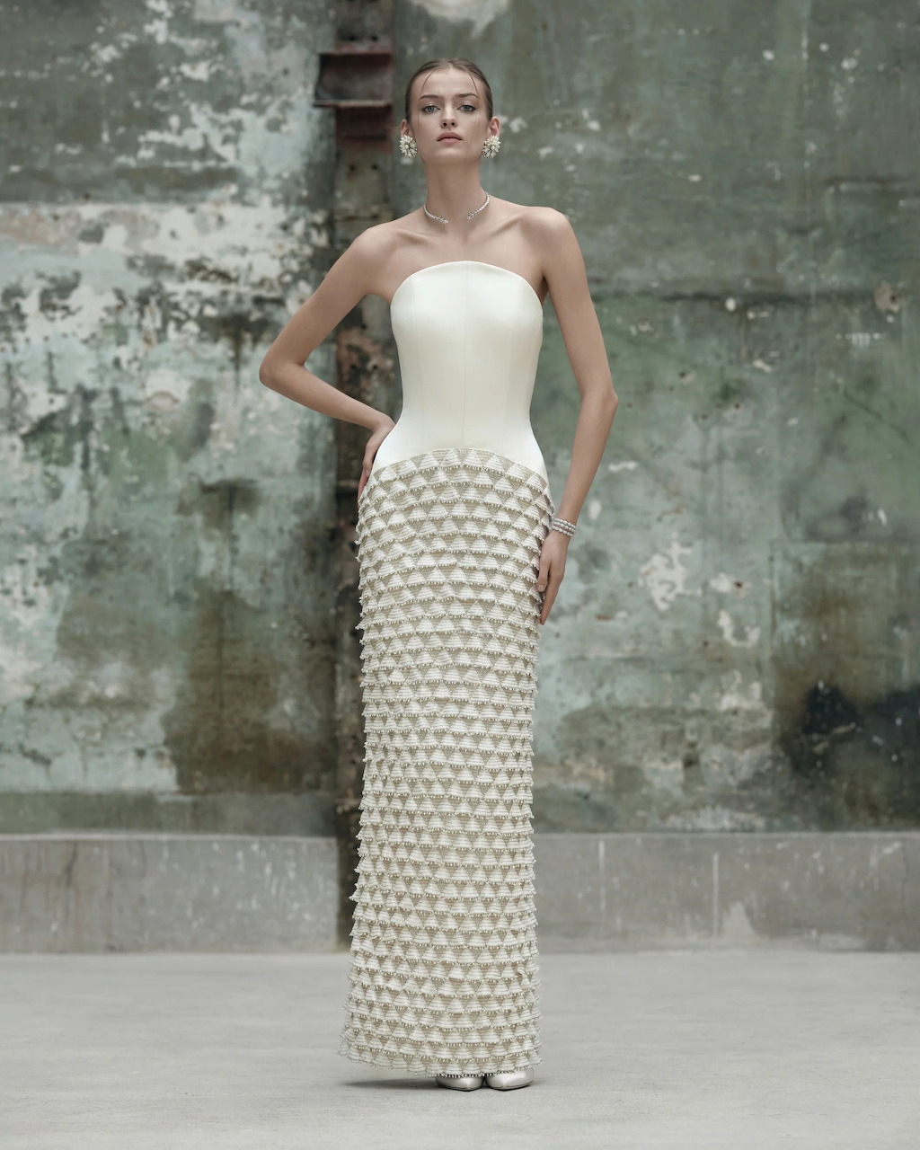 Woman in white strapless bridal gown with geometric textured skirt against distressed concrete background