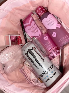 Pink bag containing Monster energy drink, pink beauty products, and accessories in a pastel aesthetic flatlay