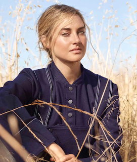Blonde woman in navy jacket standing among tall dry golden grass outdoors