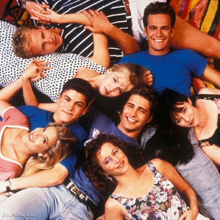Six smiling young adults lying together in a close group portrait, viewed from above