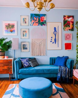Retro living room with a blue sofa, ottoman, framed wall art, and wooden floor