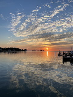 Colorful sunset over calm harbor water with cloud reflections and a dock with boats on the right