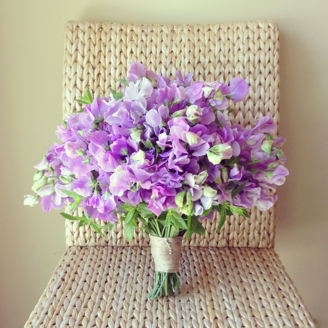 Purple and lavender sweet pea flower bouquet tied with white ribbon on wicker chair