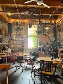 Rustic café interior with brick walls, wooden furniture, vintage hanging décor, and patrons seated at tables