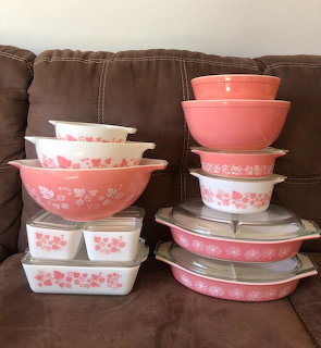 Stack of vintage pink Pyrex bowls and containers with white gooseberry floral pattern on brown couch