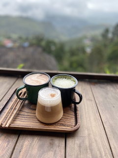 Three coffee mugs on a wooden tray on a deck with misty mountain scenery in background