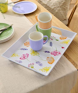 Breakfast table with colorful mugs, plates, and fruit-decorated tray on wood surface