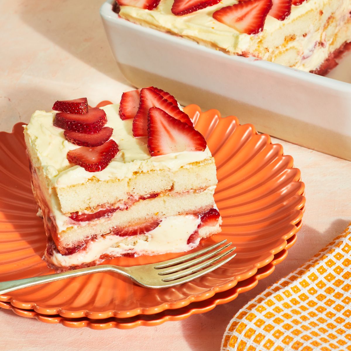 Slice of strawberry cream layer cake on an orange plate with a fork